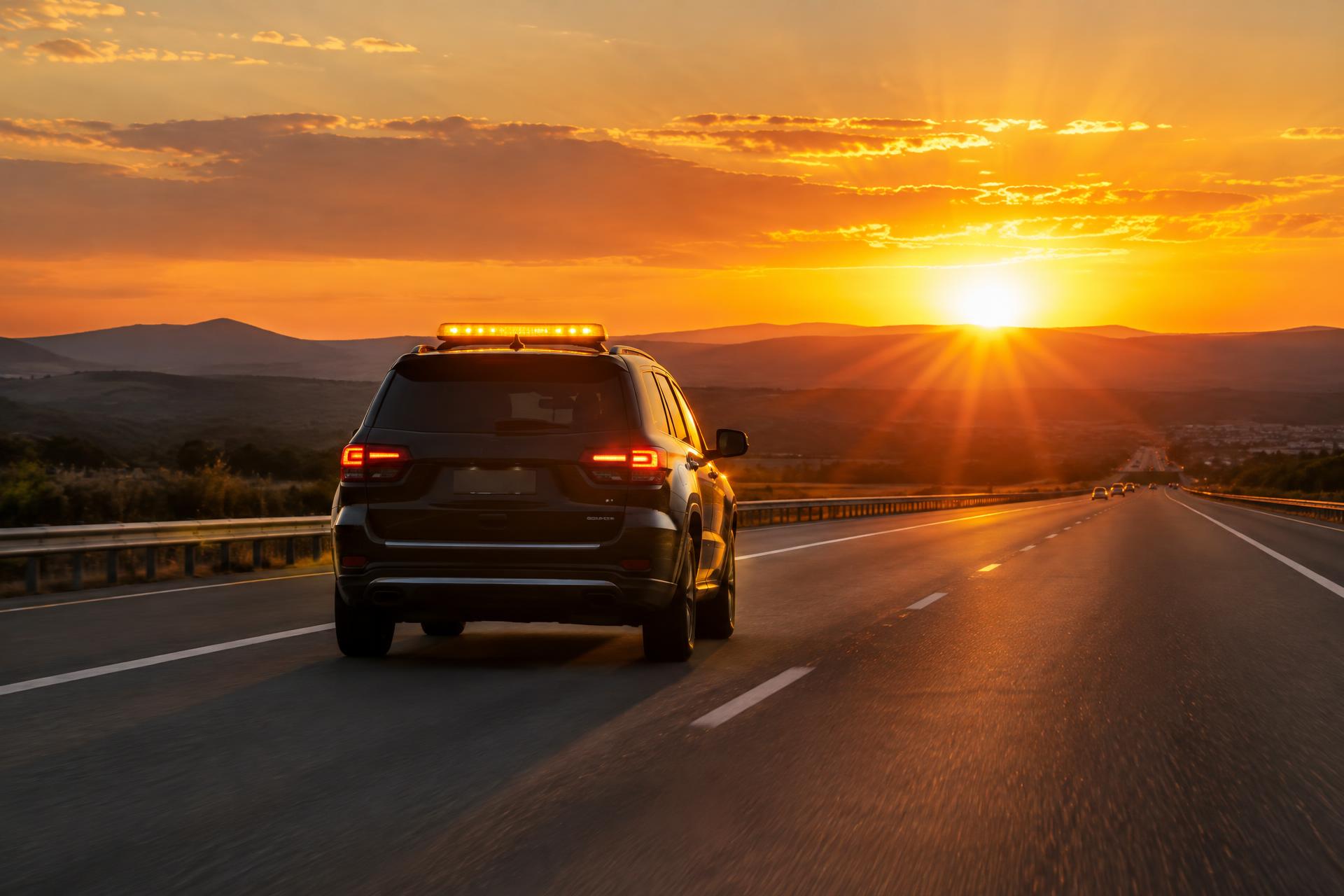 A car with a glowing rooftop display driving into a golden sunset on an open highway